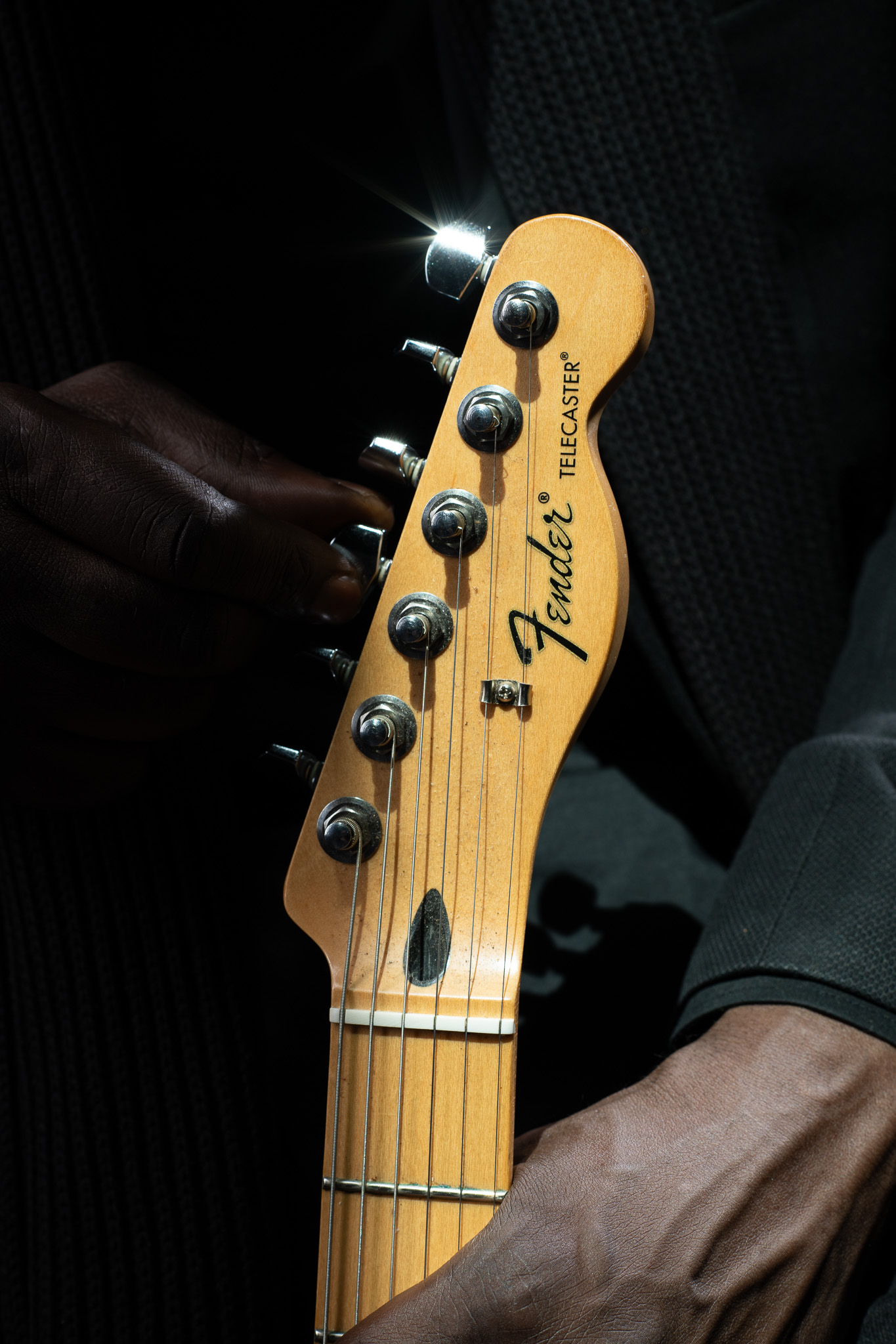 Kyazi Lugangira’s hands resting around the headstock of a Fender Telecaster guitar