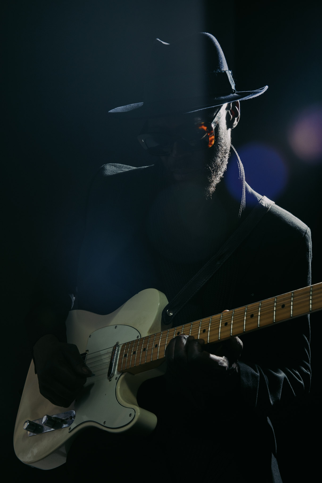 Kyazi Lugangira holding a white Fender Telecaster in deep shadow and rim light