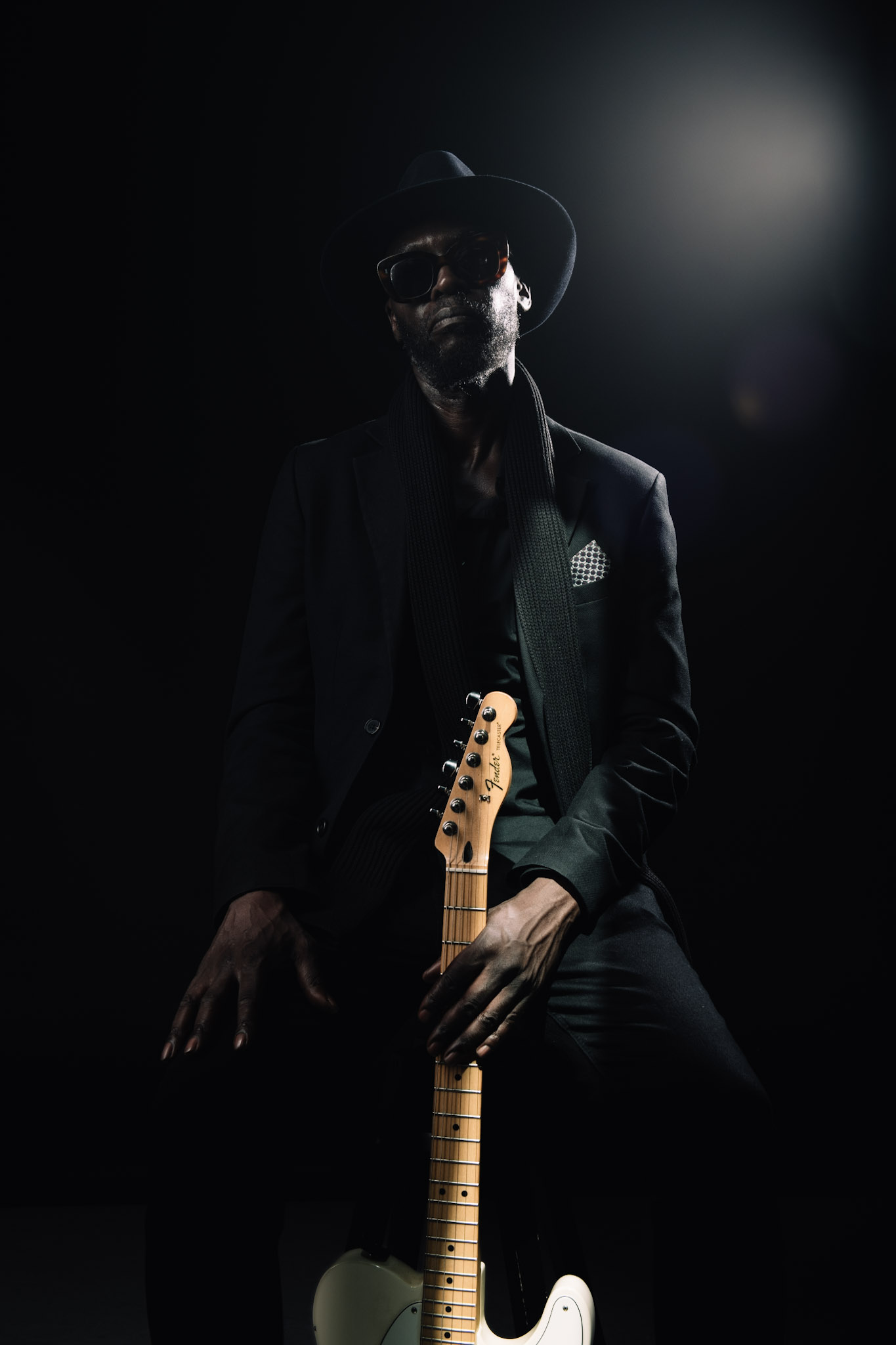 Kyazi Lugangira seated with a Fender Telecaster beneath a studio spotlight