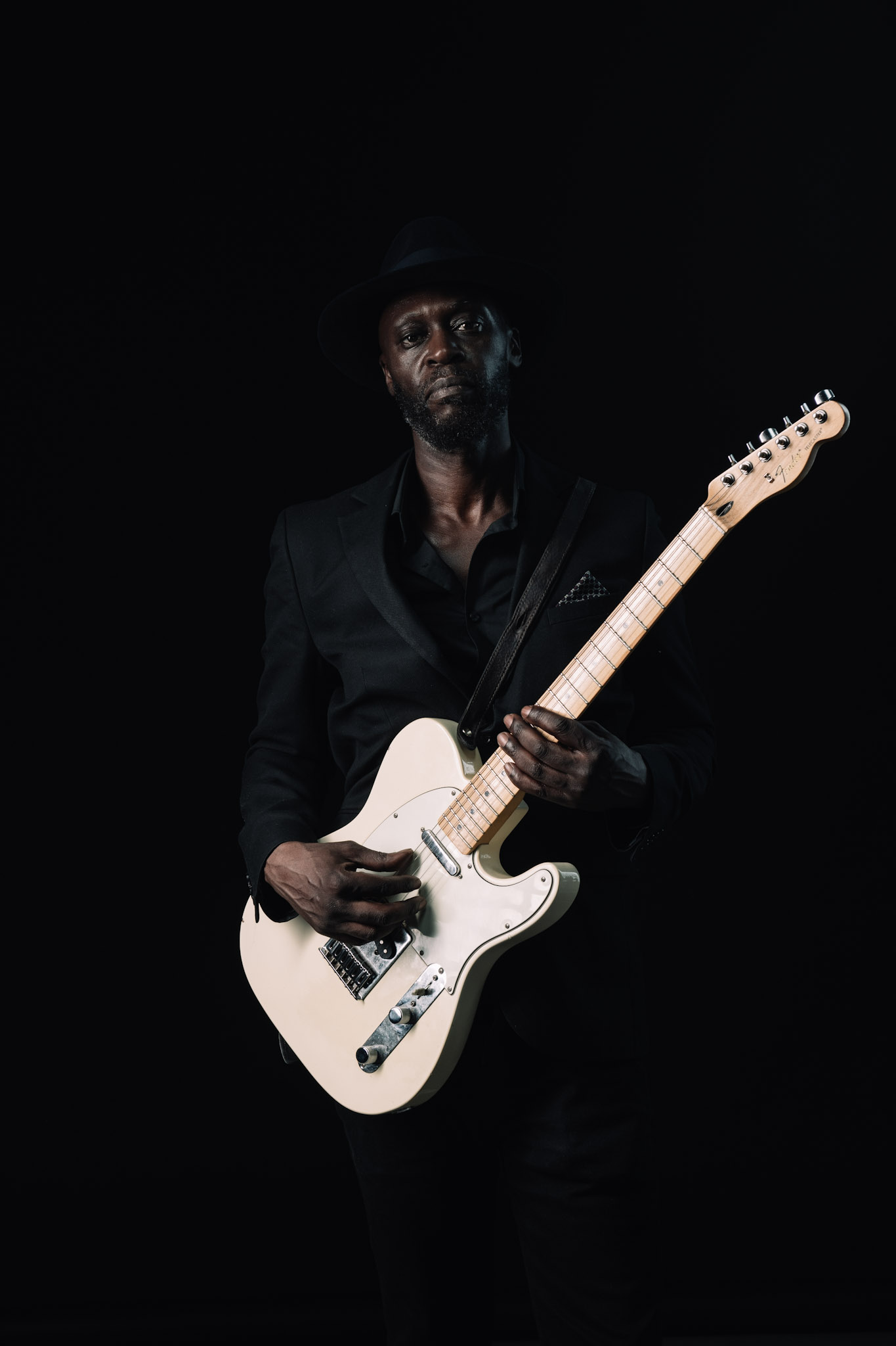 Kyazi Lugangira holding a white Fender Telecaster against a black background