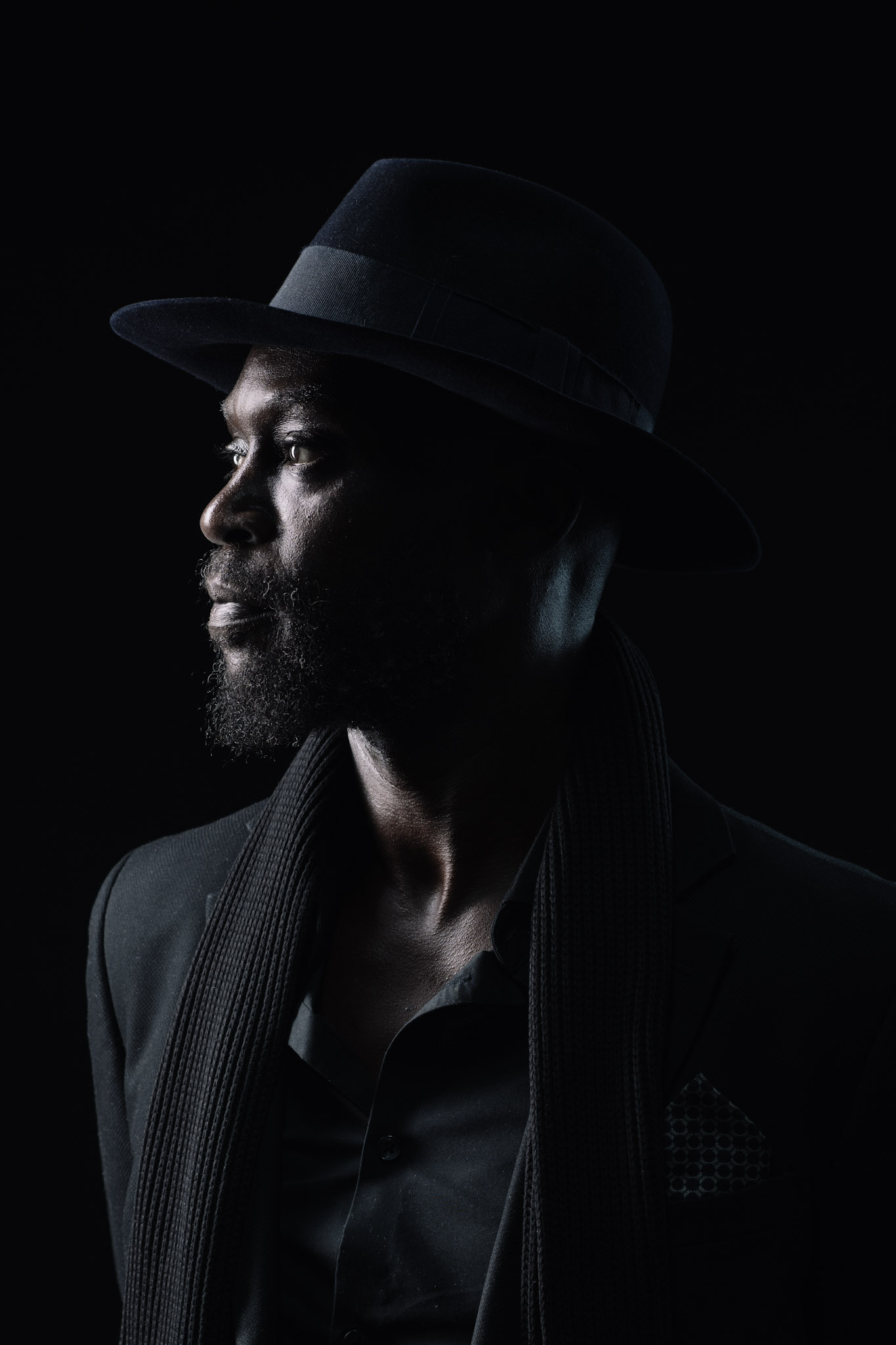 Side-profile portrait of Kyazi Lugangira in a black hat with rim light