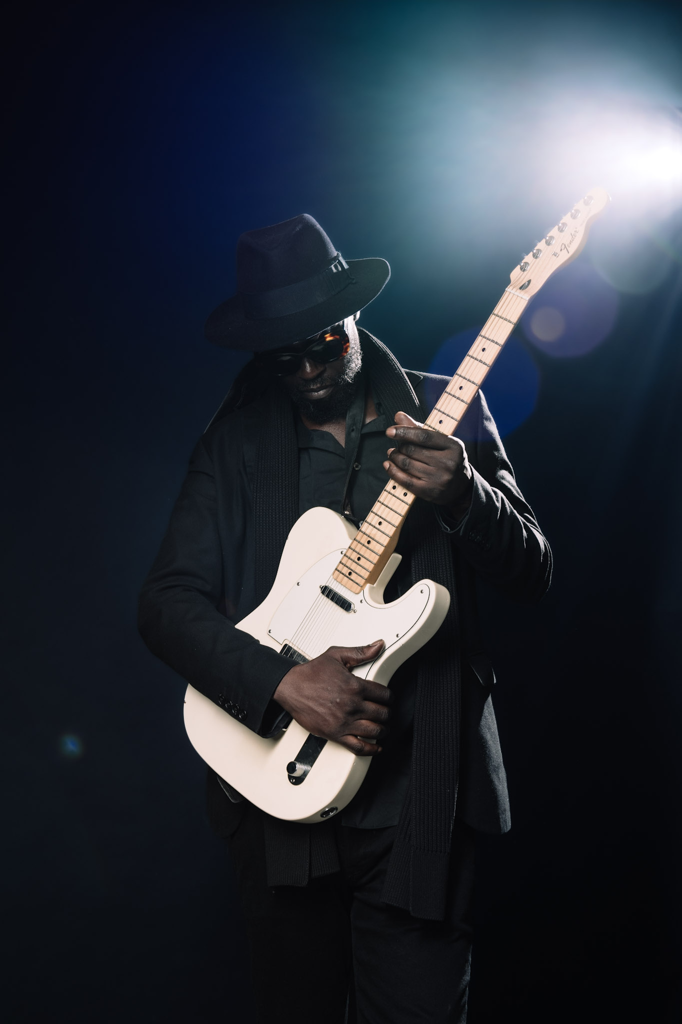 Kyazi Lugangira holding a white Fender Telecaster in blue-green backlight