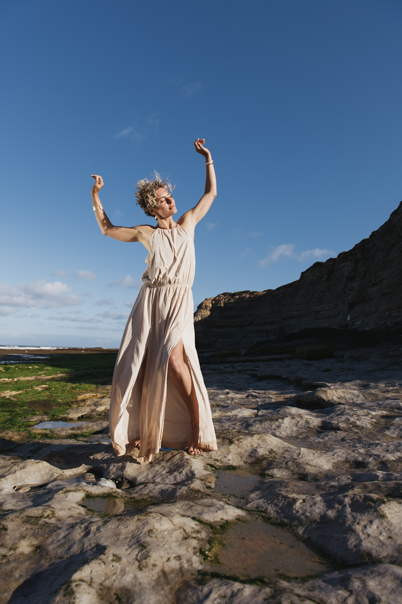 Woman in a flowing ivory dress moving across the rocky Portugal coast
