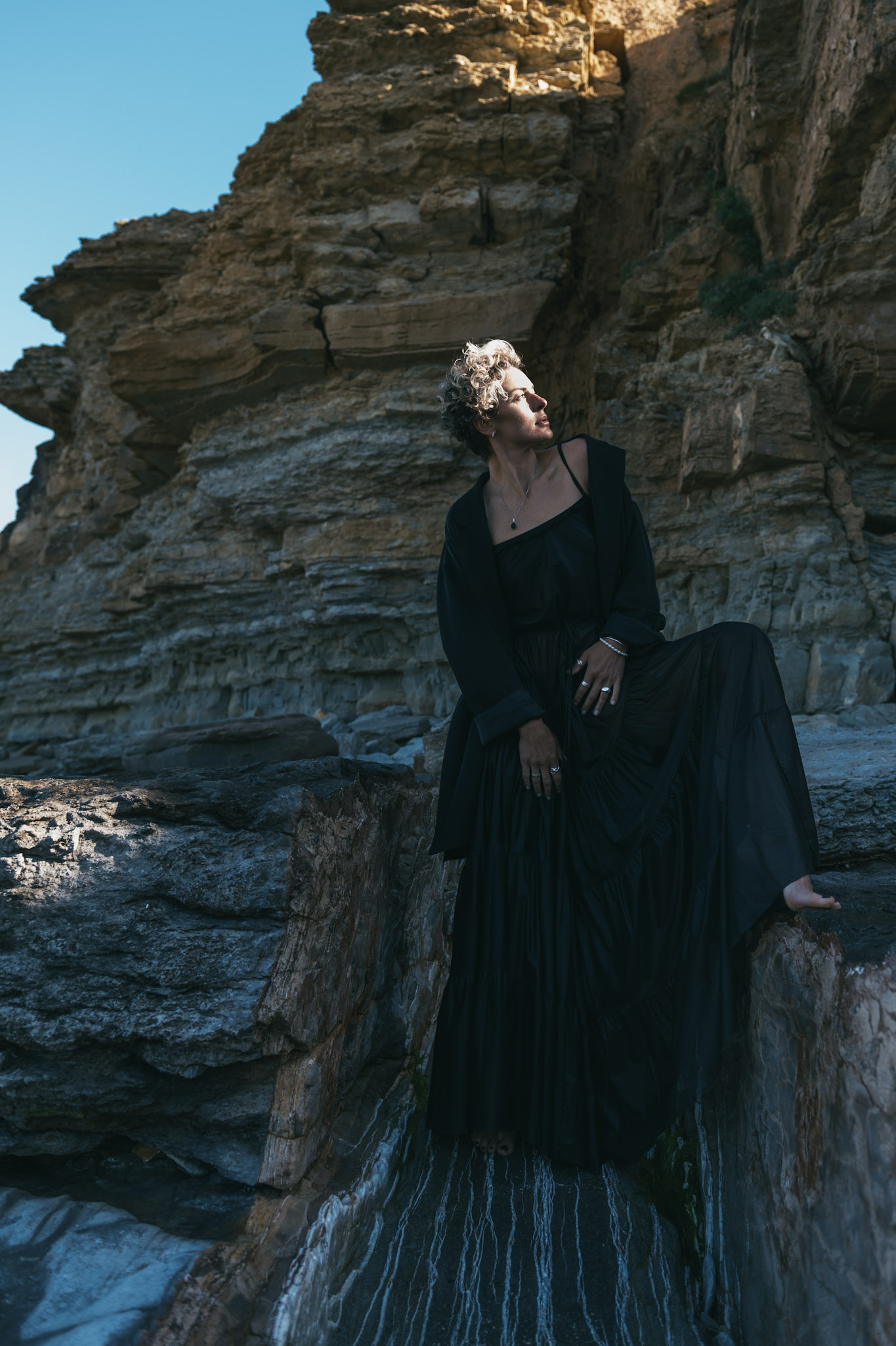 Woman in a black dress posed against layered coastal cliffs