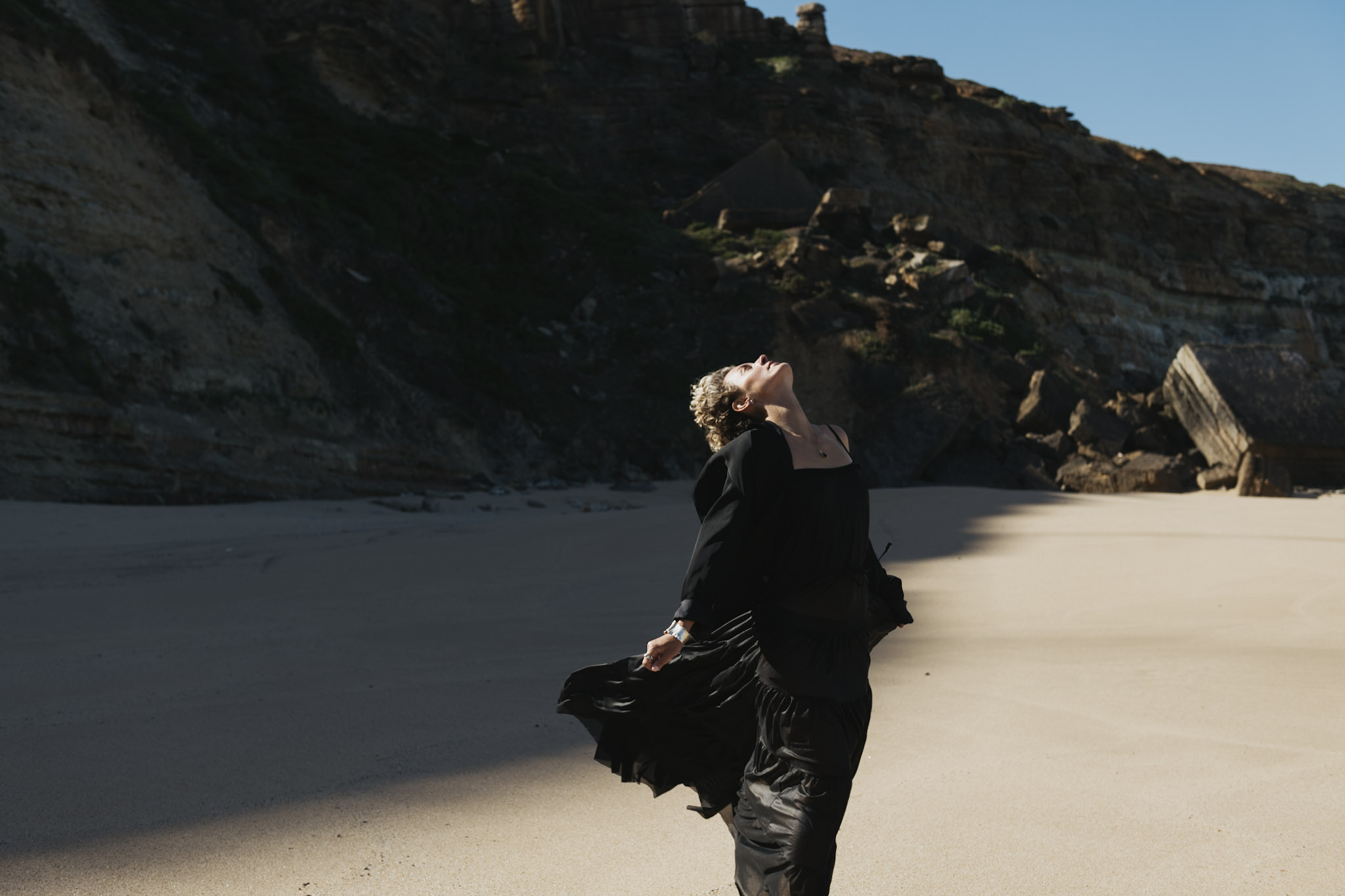 Woman in a black dress leaning into sunlight on a secluded beach in Portugal