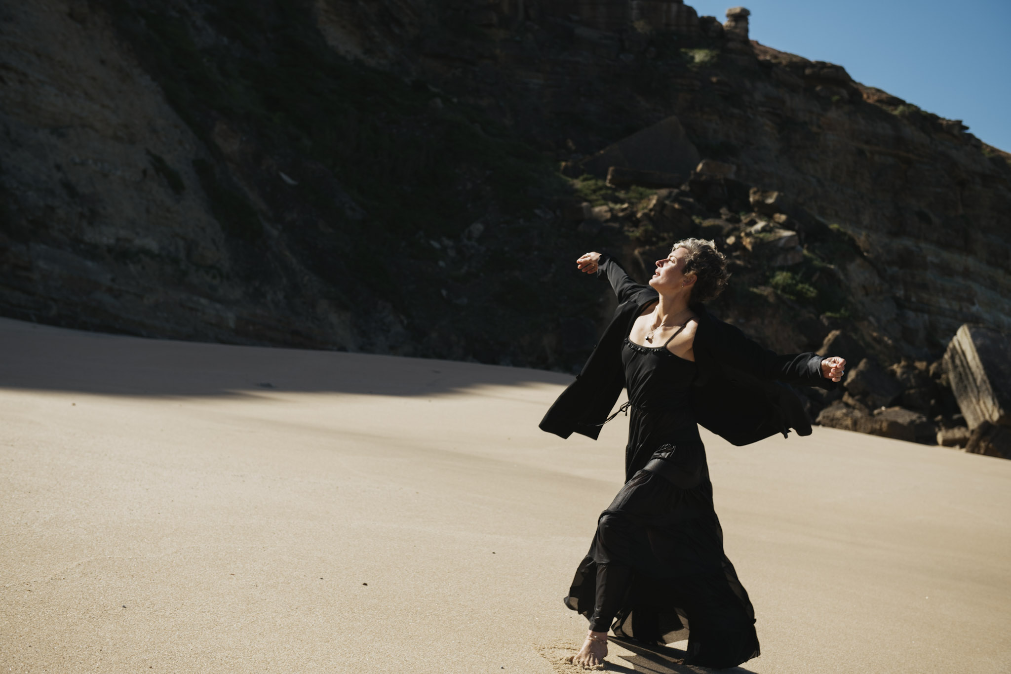 Wide portrait of a woman dancing in a black dress on a Portugal beach